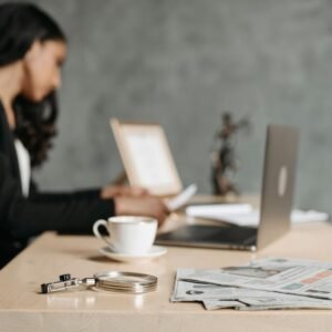 A woman in a business suit working at a desk with a laptop and papers in an office.