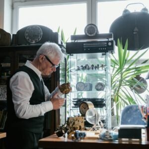Elderly man repairing clocks in a workshop surrounded by timepieces and tools.